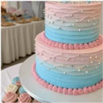 Ombre pink and blue gender reveal cake decorated with vanilla buttercream, edible pearls, and piped frosting for a baby shower celebration.