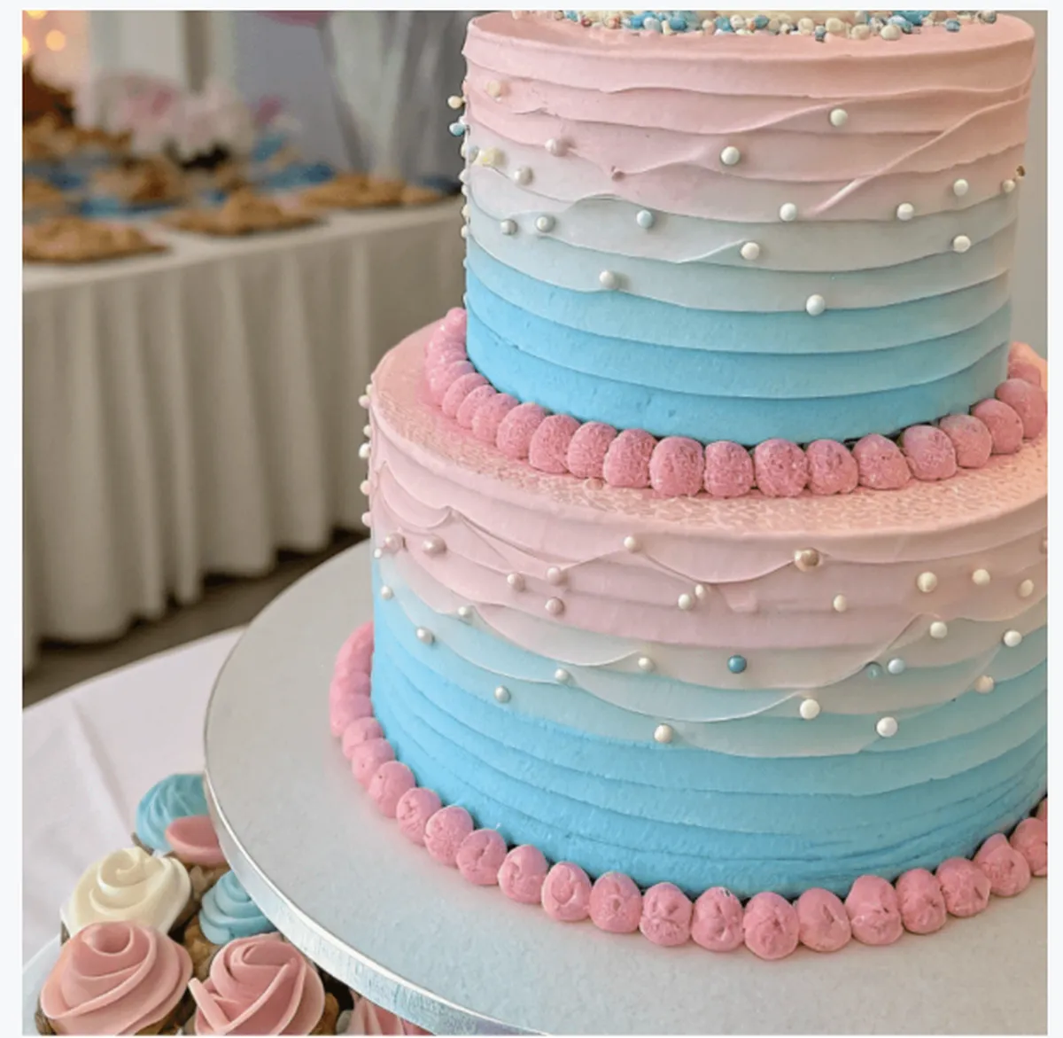 Ombre pink and blue gender reveal cake decorated with vanilla buttercream, edible pearls, and piped frosting for a baby shower celebration.